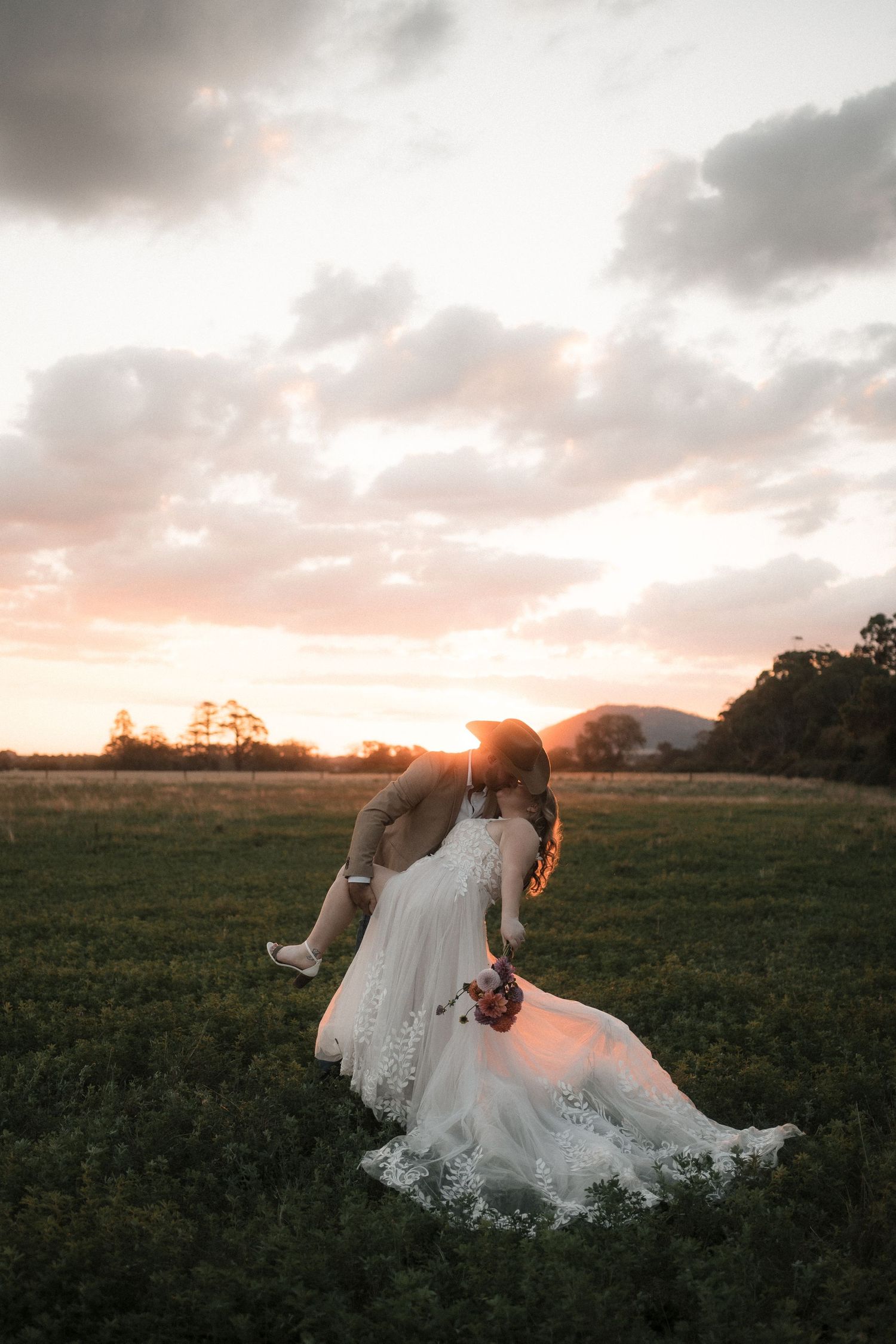 White wedding dress flowing gracefully across a grassy field during a dreamy sunset photoshoot.