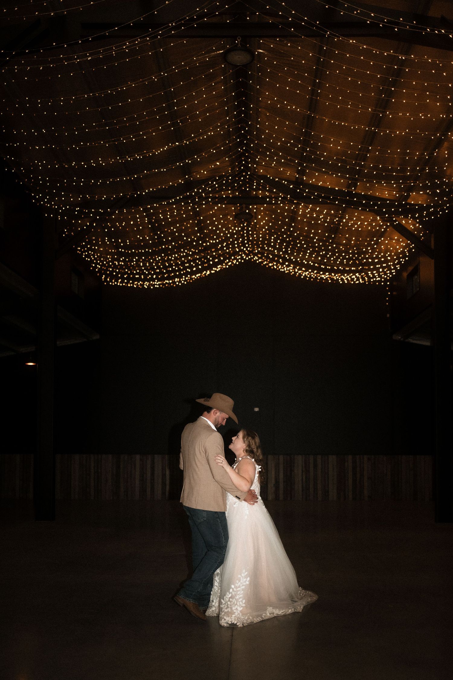 String lights create a romantic canopy over a dimly lit dance floor at an evening celebration.