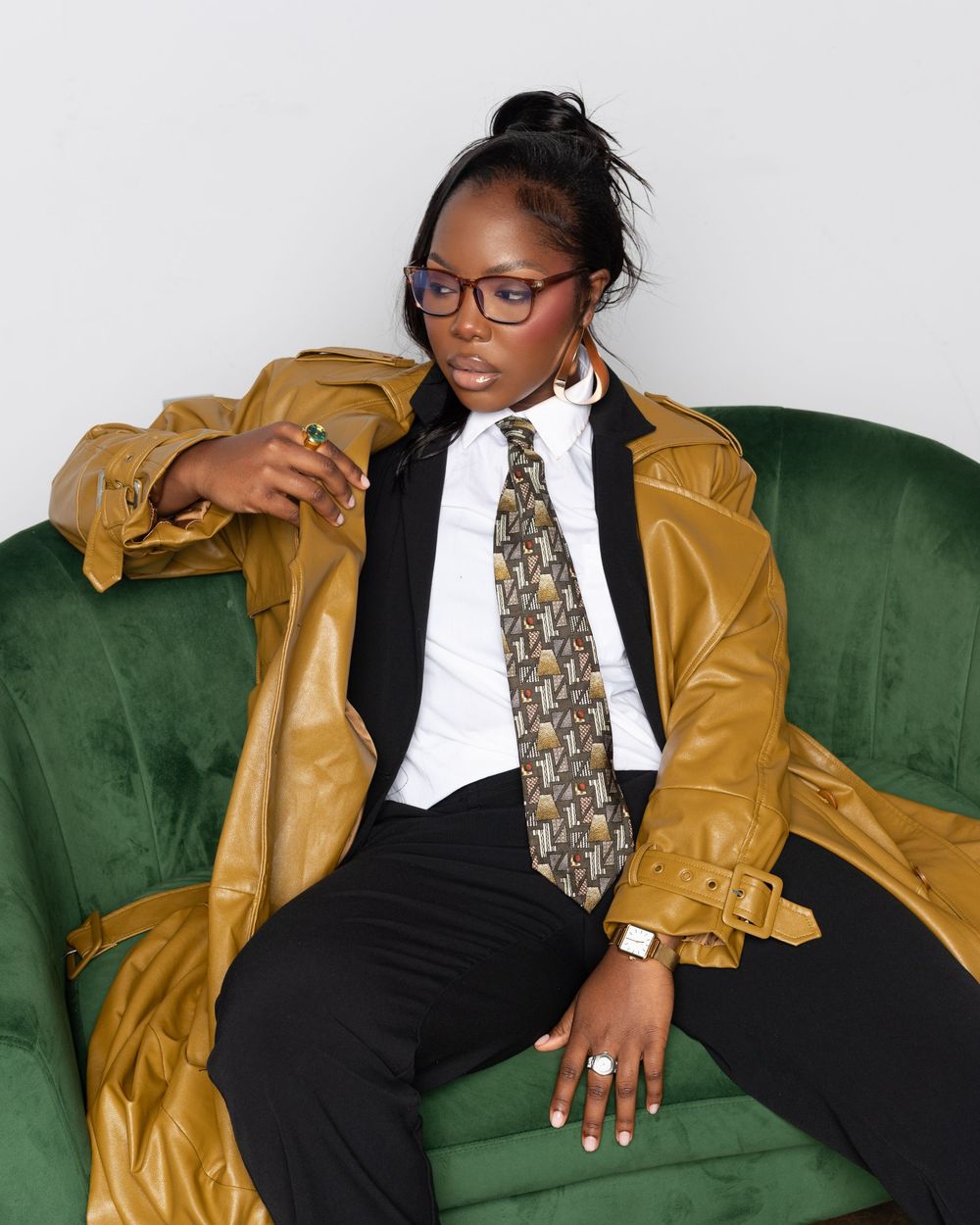 Stylish fashion poses on a green velvet couch featuring a mustard jacket, black suit and patterned tie ensemble.