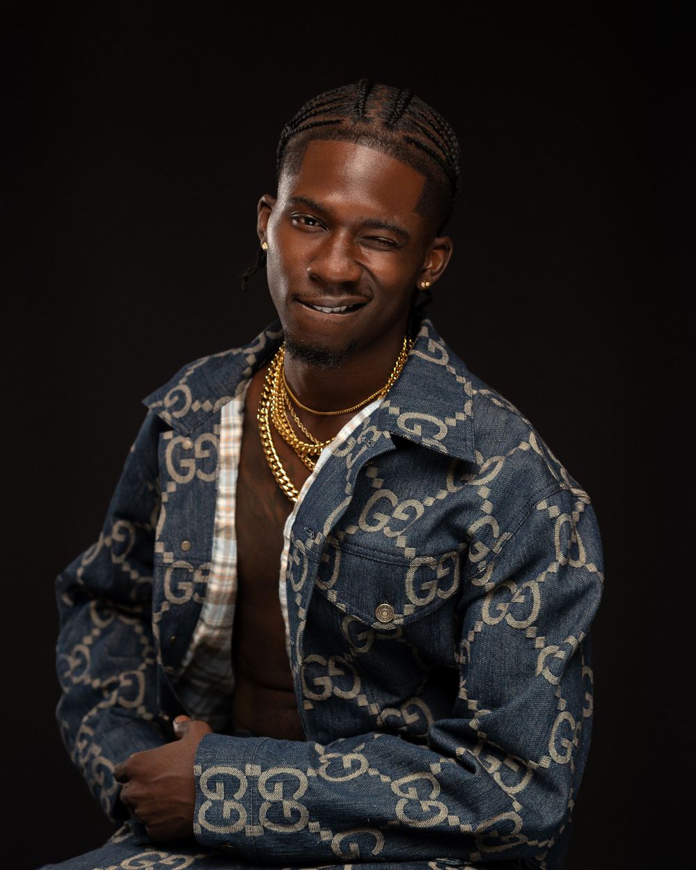 A person wearing a denim jacket with repeating monogram pattern poses against a dark background in multiple shots.