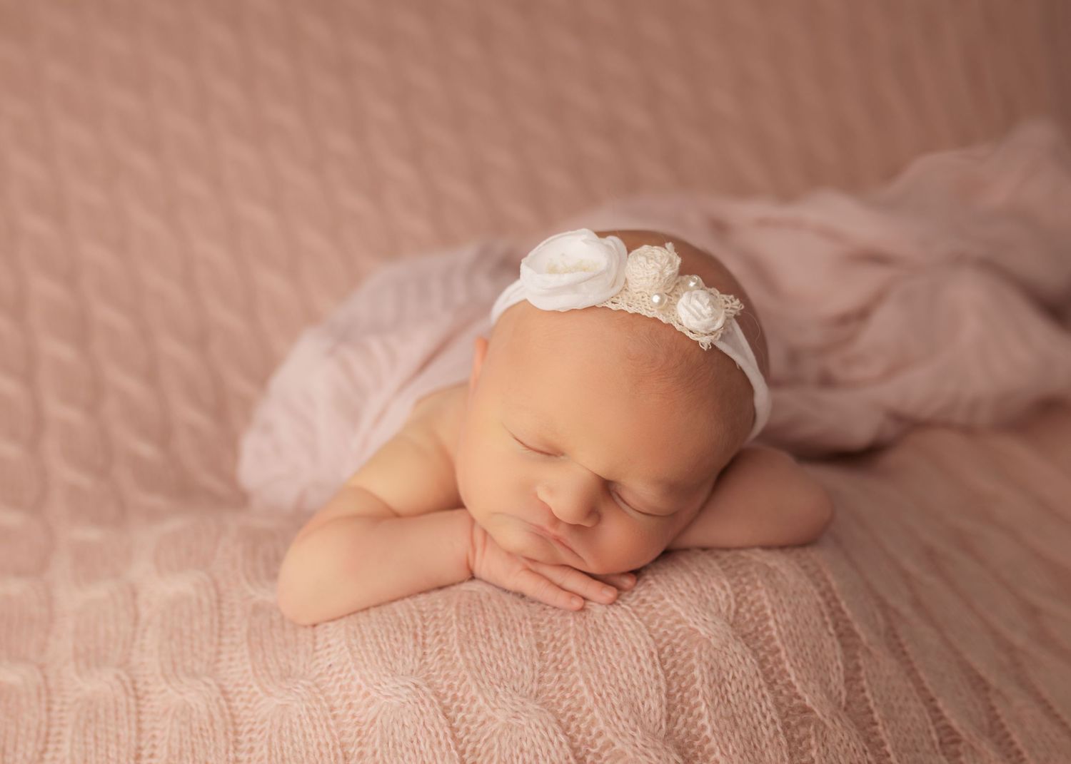 A sleeping baby wearing a white headband rests peacefully on a red surface in warm lighting.