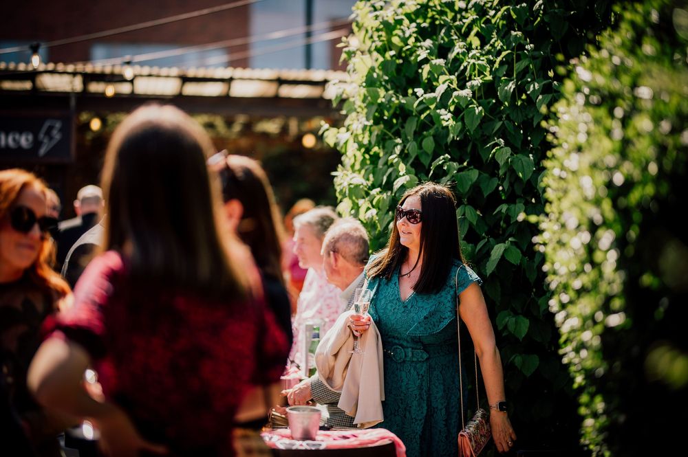 Wedding guests enjoying drinks and conversation at an outdoor reception under string lights and greenery.