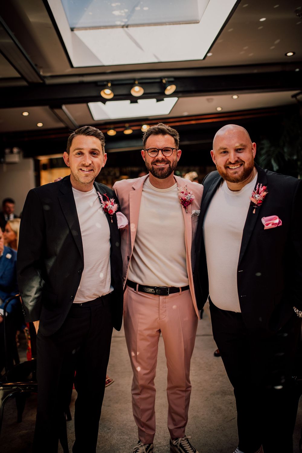 Group of people wearing formal attire pose together at an indoor event with modern lighting.