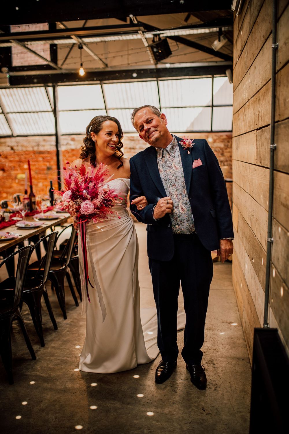 A couple shares a joyful moment dancing together in an industrial-style venue with brick walls and wooden beams.