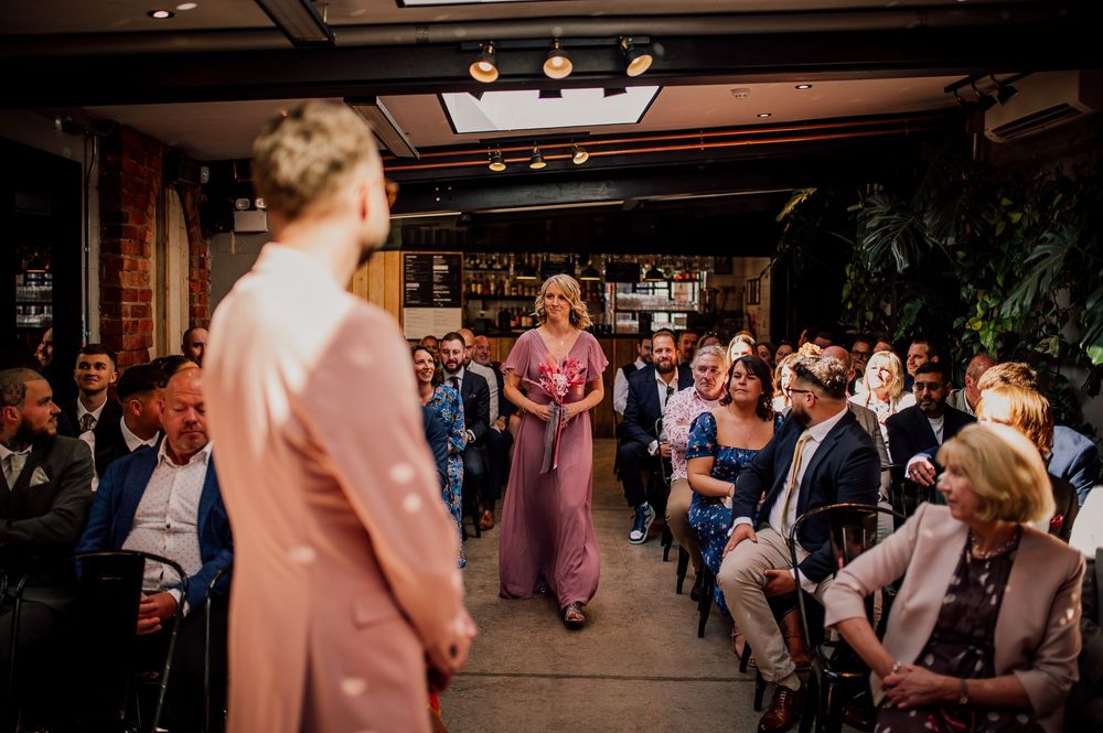 Wedding guests dance and celebrate on a dimly lit dance floor at an indoor reception venue.
