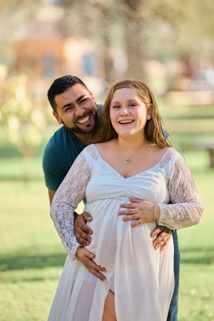 A couple embraces in a sunny outdoor setting with soft natural lighting and green grass in the background.