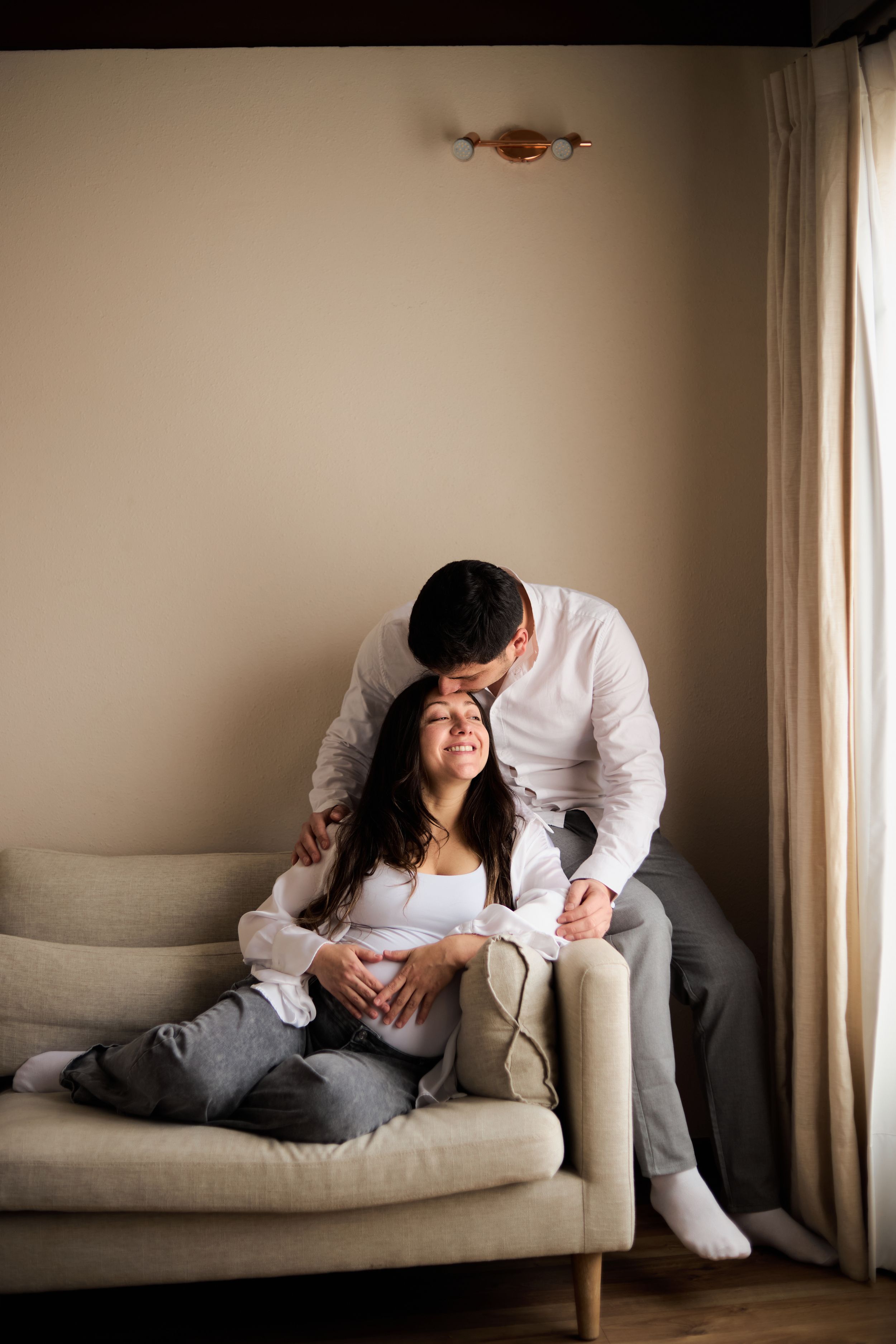 A series of four intimate photos showing two people in tender moments on a light gray couch near a window.