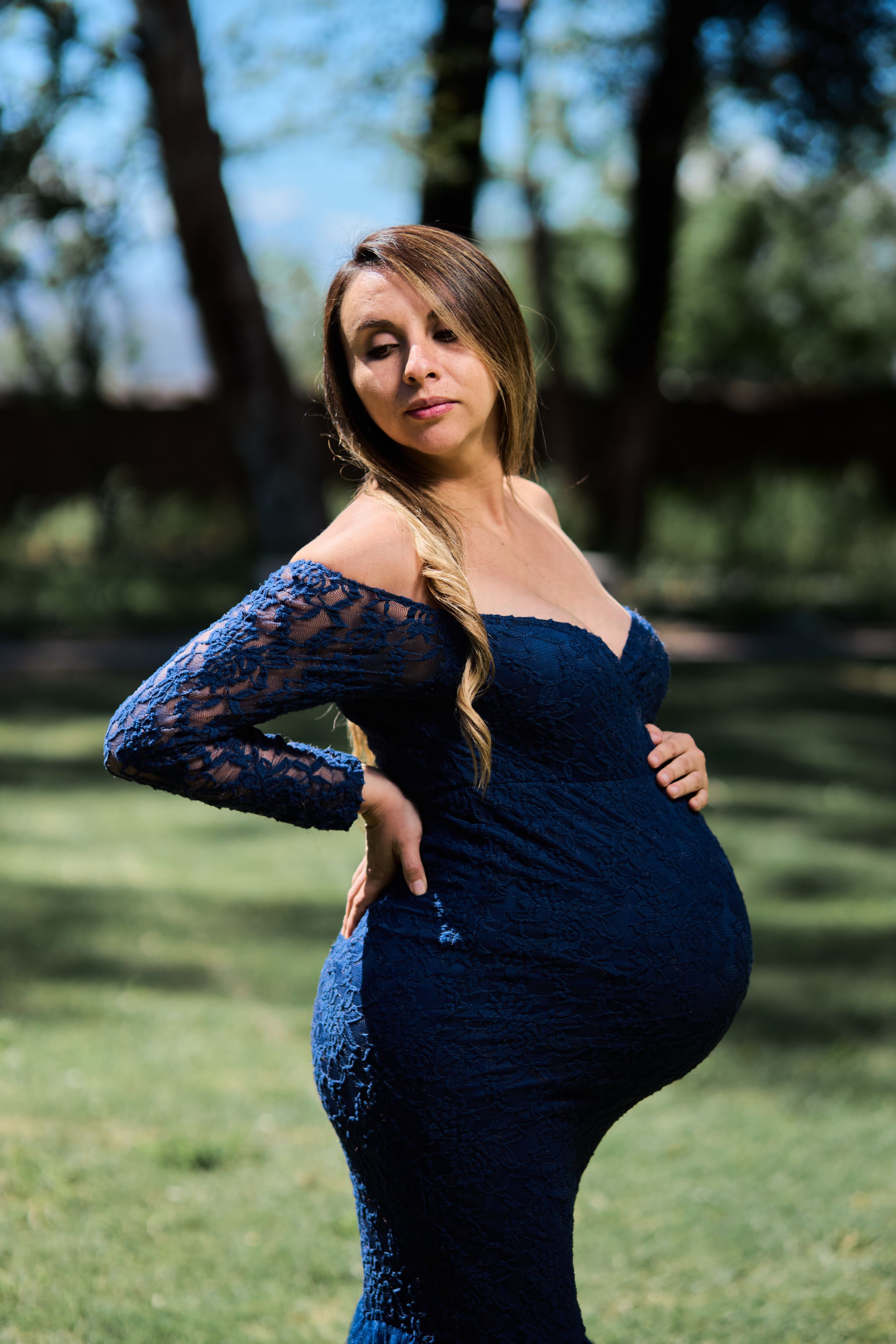 A figure in a navy blue lace dress poses gracefully outdoors against a natural background.