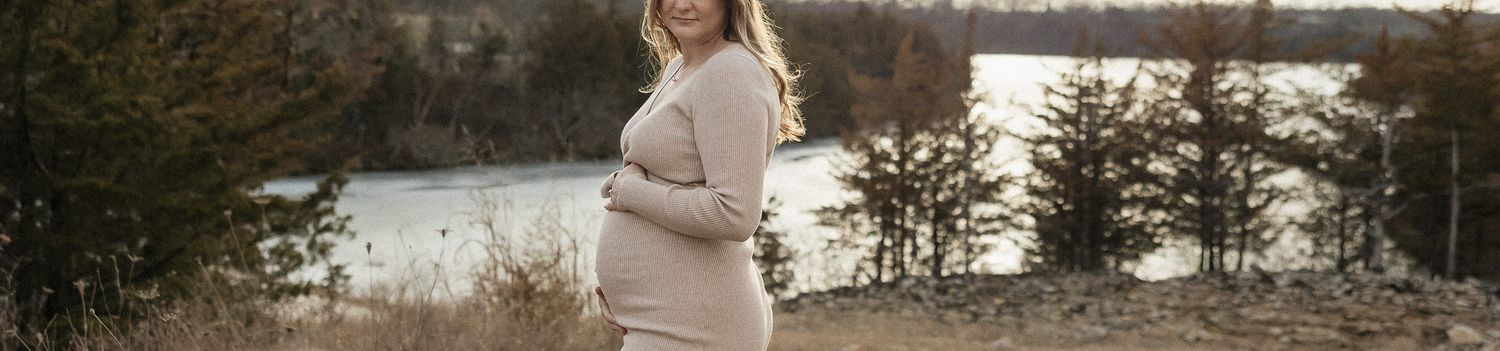 pregnant mother to be holder baby bump in front of a lake during photo session as date night ideas in kansas city