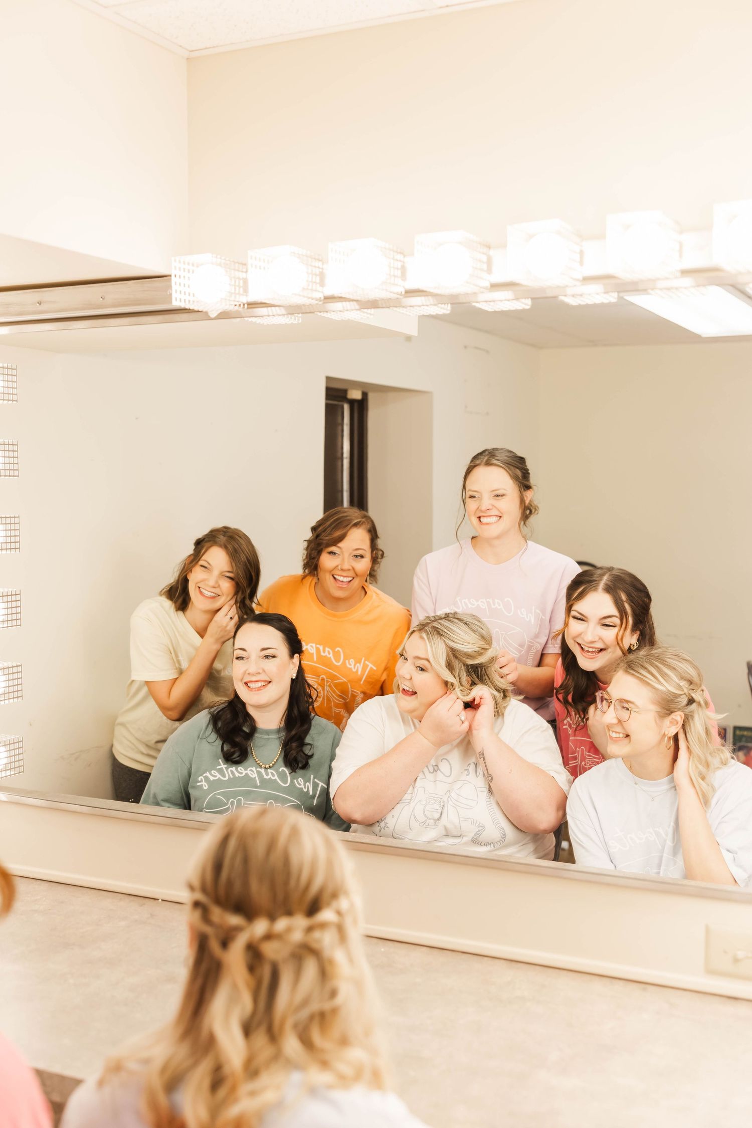 bride and bridesmaids getting ready in front of mirror smiling