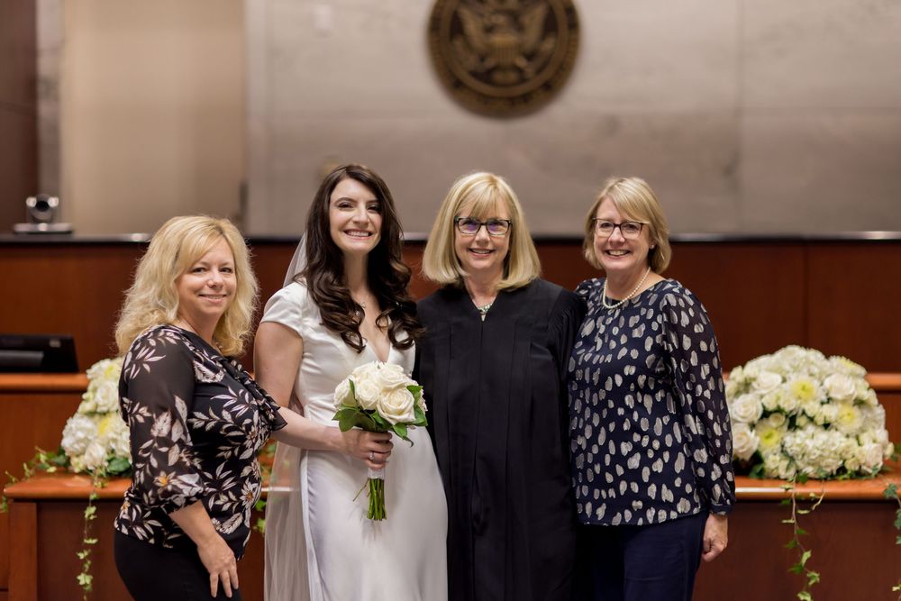 Group gathered in formal attire at a courthouse ceremony with floral arrangements.