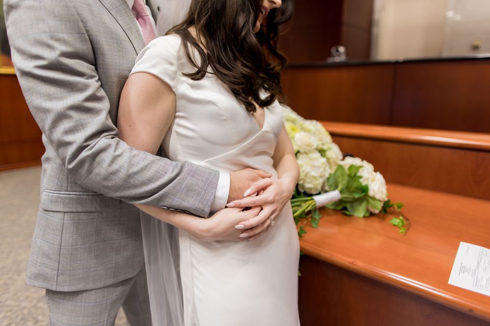 A couple embraces during their courthouse wedding ceremony while wearing formal attire.