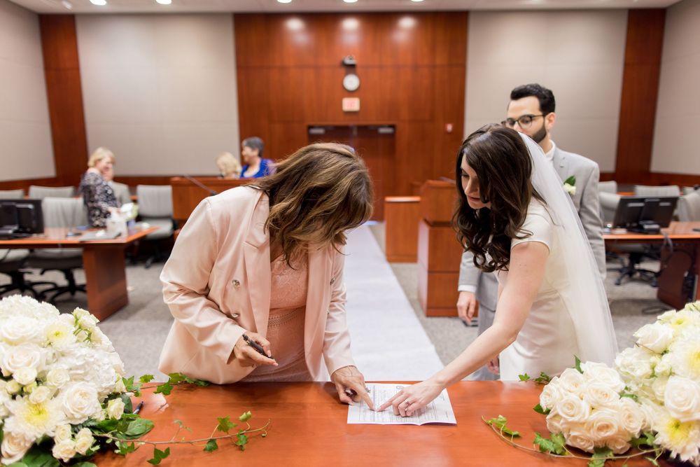 A group signing documents at a conference table decorated with floral arrangements in a wood-paneled meeting room.