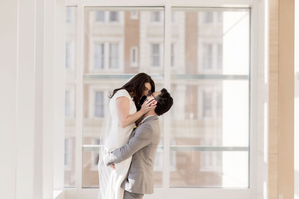 A romantic moment shared between newlyweds in a sunlit courthouse corridor.