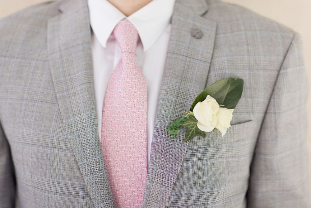 Groomsmen in matching light gray suits with pink ties and white boutonnieres stand together at a formal event.