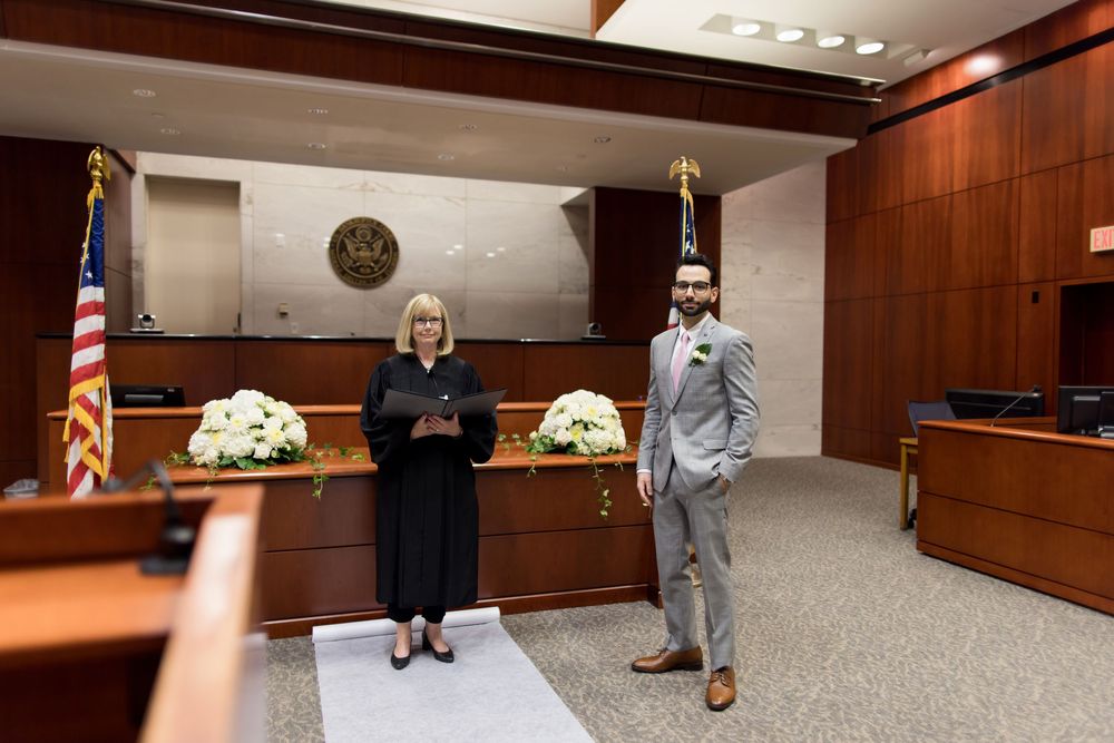 Wood-paneled courtroom interior with American flag and seal showing traditional legal proceedings setup.