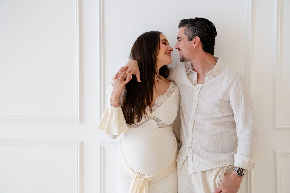 Romantic couple in white clothing sharing intimate moments in a bright minimalist setting.