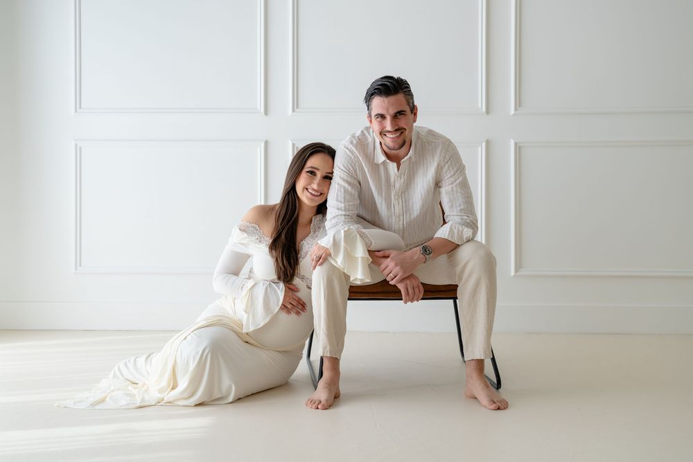 A romantic couple in white clothing poses together in a bright minimalist studio setting for wedding photos.