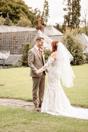 A couple shares joyful reactions during their first look on a grassy lawn with buildings in the background.
