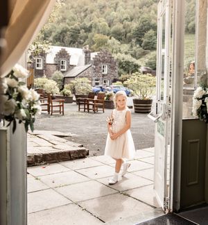 Young child in white dress playing on an outdoor stone patio with French doors and garden furniture.