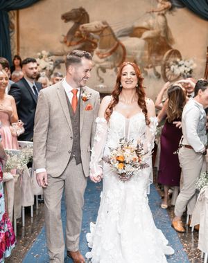 A couple walks down the aisle at their wedding ceremony while guests look on with a decorative mural in the background.