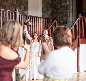 Wedding guests gather on a rustic porch with wooden railings to take photos.