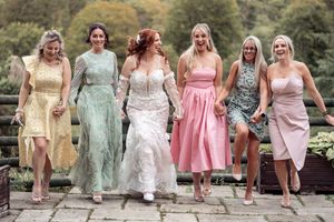 Bridesmaids in pastel dresses sit together on wooden steps during an outdoor wedding photo session.