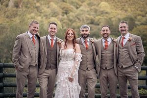 Wedding party poses outdoors with groomsmen in gray suits and colorful ties against natural backdrop.