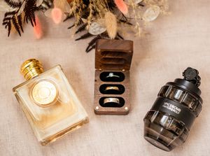 Wedding accessories including perfume bottles and ring boxes arranged on a light linen surface.