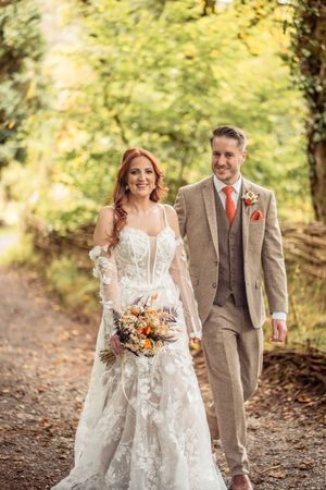A couple walks together on a wooded path during an autumn wedding photoshoot.