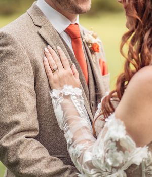 Close-up shot of a couple's hands with a white lace sleeve and tweed jacket during a romantic outdoor moment.