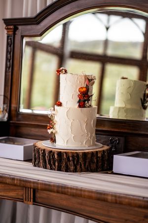White wedding cake with delicate swirl patterns sits on rustic wood slice against elegant dark wooden backdrop.