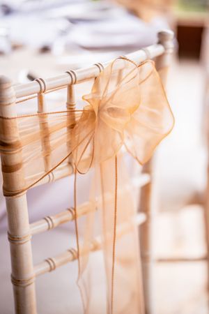 A delicate peach organza bow tied to a white Chiavari chair for wedding decor.