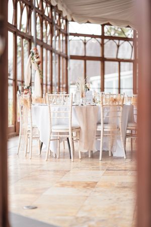 Empty wedding reception venue with white tables and chairs arranged in rows beneath elegant columns.