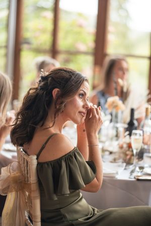 Wedding guests react emotionally during reception speeches in an elegant venue with large windows.
