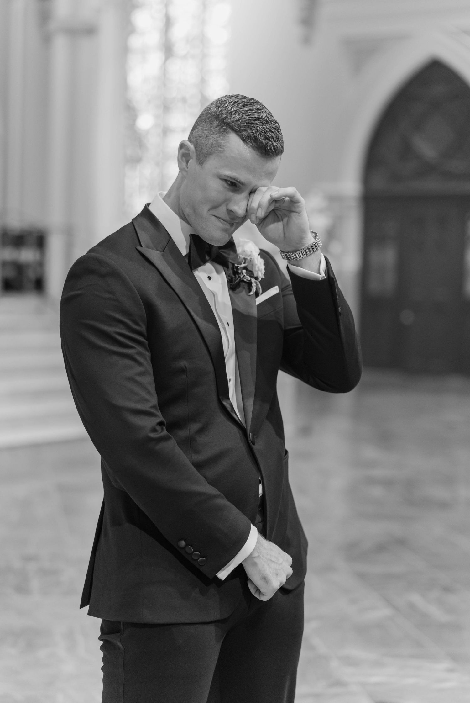 A series of black and white photos showing a groom in a formal tuxedo striking emotional poses in an elegant venue.