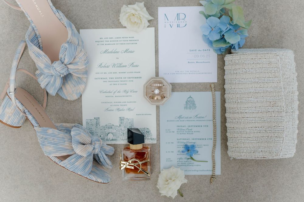 Wedding invitation suite with blue and cream floral details displayed on a light gray textured background.