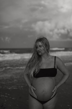 A black and white photo series shows someone posing on a beach with dramatic cloudy skies in the background.