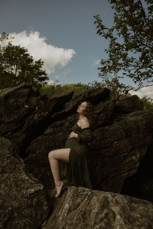 A person in dark clothing reclines on a rocky outcrop against a cloudy sky in a moody nature scene.