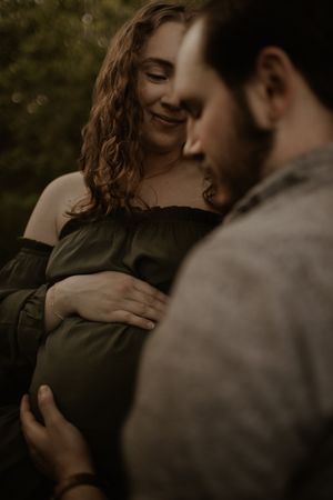 A romantic couple shares an intimate moment in a moody outdoor setting with natural lighting and dark tones.