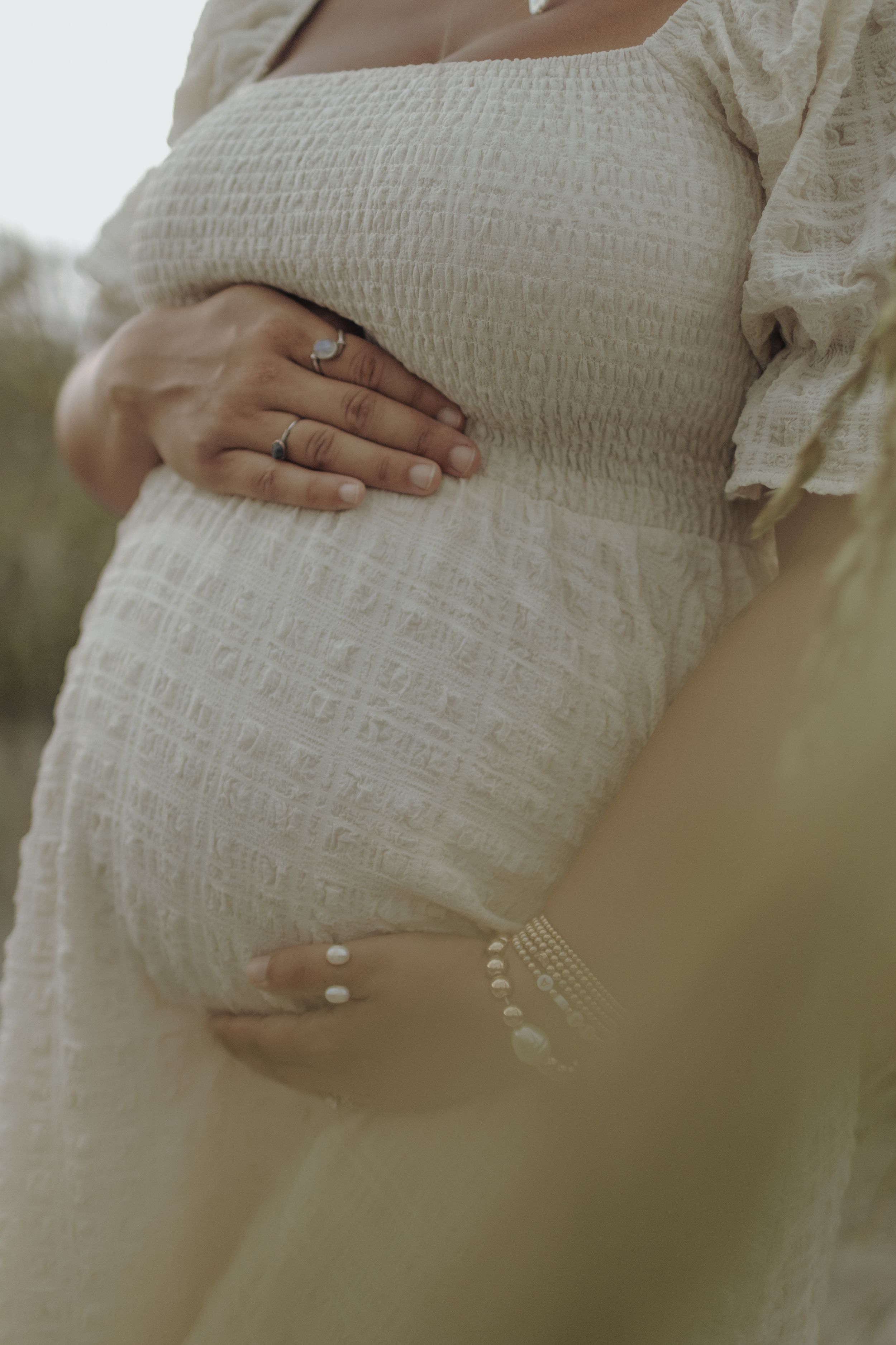 A series of maternity photos showing hands gently cradling a pregnant belly in a textured white dress against a soft background.