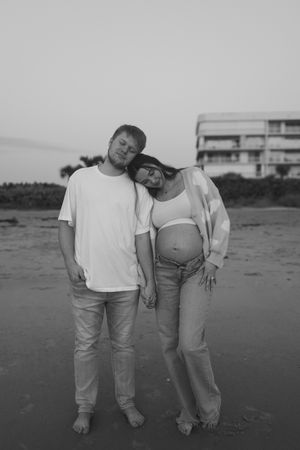Black and white photo series showing two people in casual white and gray clothing posing playfully on a beach.