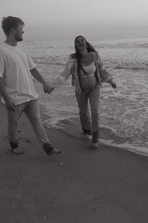 A couple holds hands while walking along a misty beach shore in black and white photography.