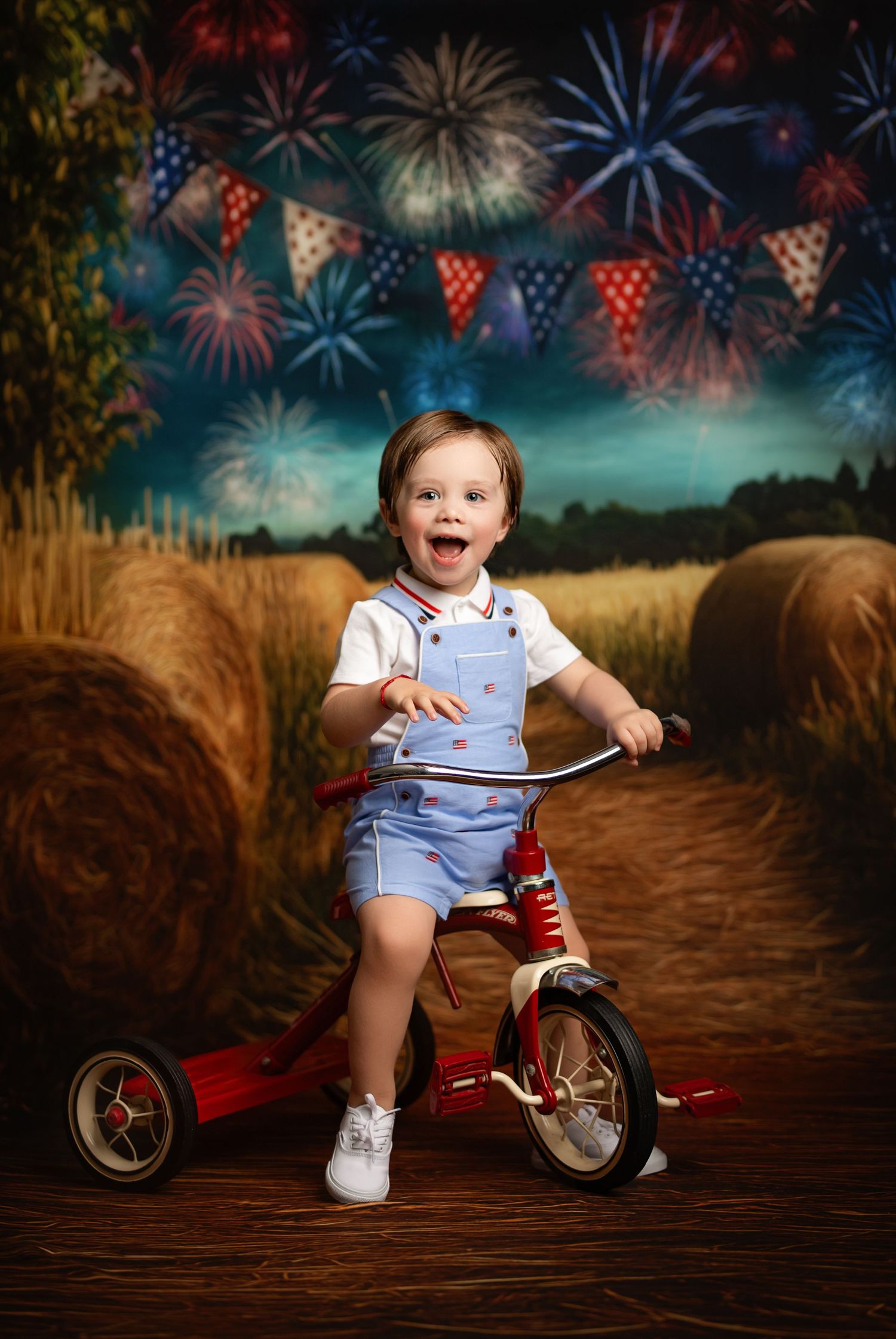 A small red tricycle sits against a backdrop of fireworks and festive bunting in a patriotic themed photoshoot setting.