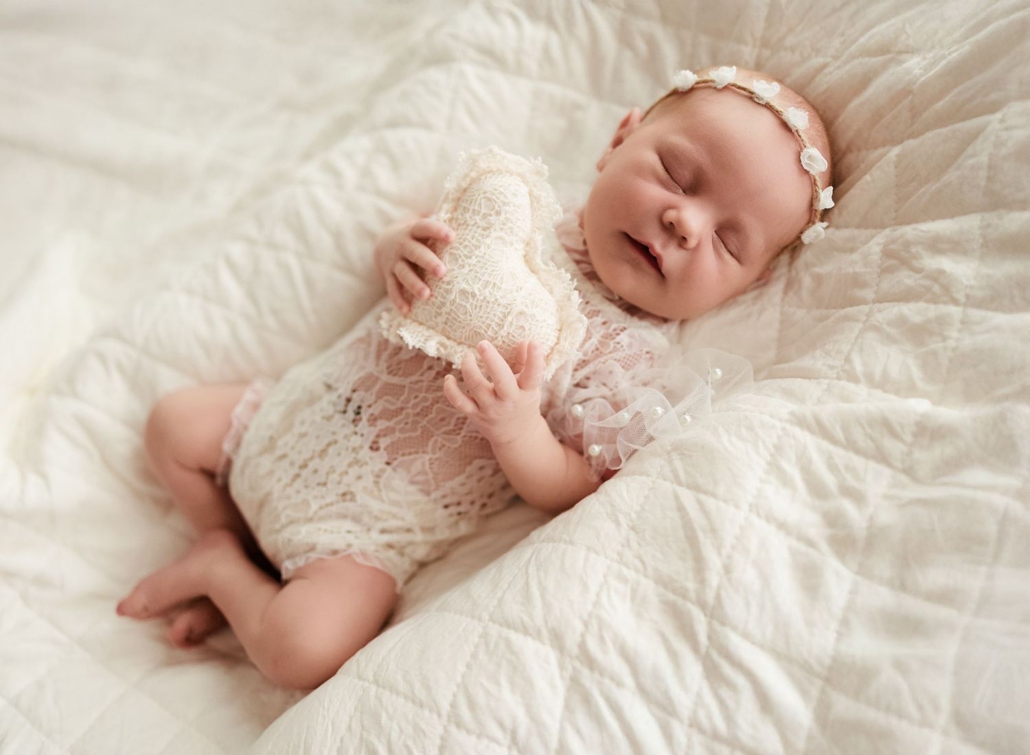 A newborn baby sleeps peacefully on soft white bedding in a series of connected photos.