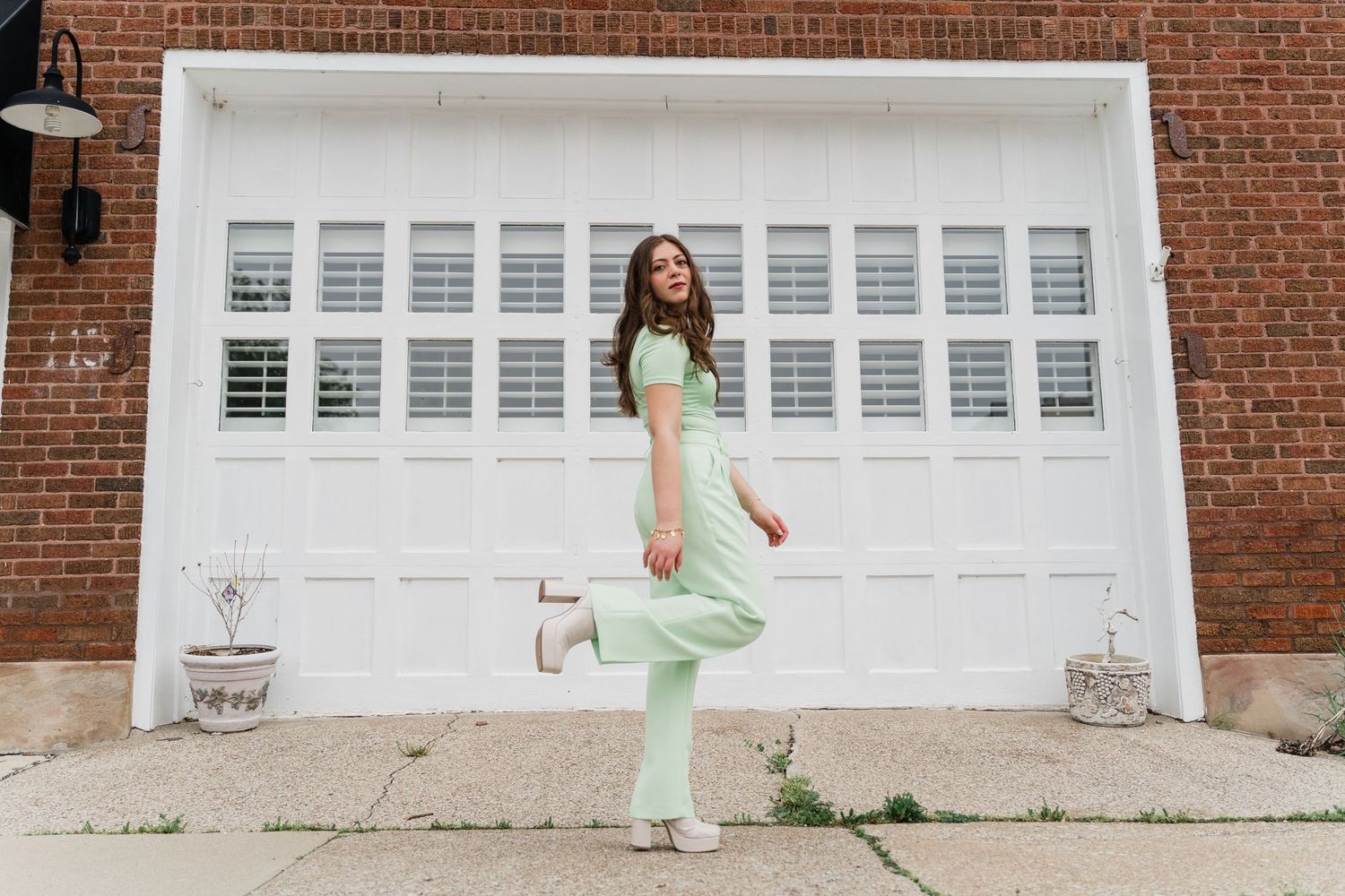 Toledo senior photos with Perrysburg student in mint green outfit poses playfully in front of white garage doors and brick walls.