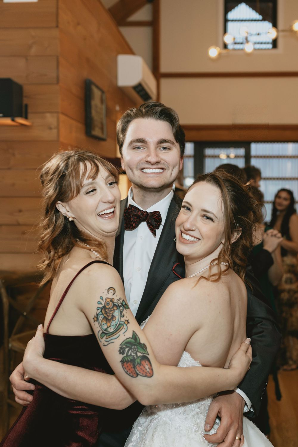 Wedding celebration with guests in formal attire embracing and laughing together at an indoor venue.