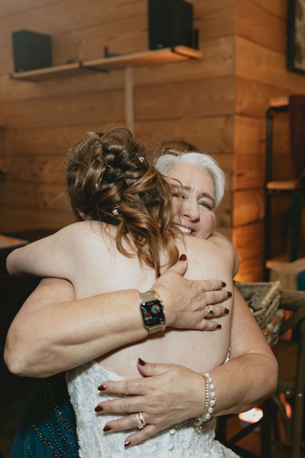 Two people sharing an emotional embrace at a wedding celebration in a wooden interior.