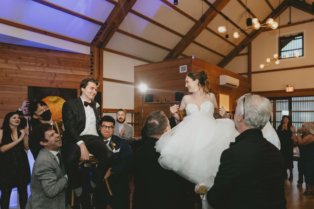 Wedding guests lift the newlyweds on chairs during a traditional celebratory dance at the reception.