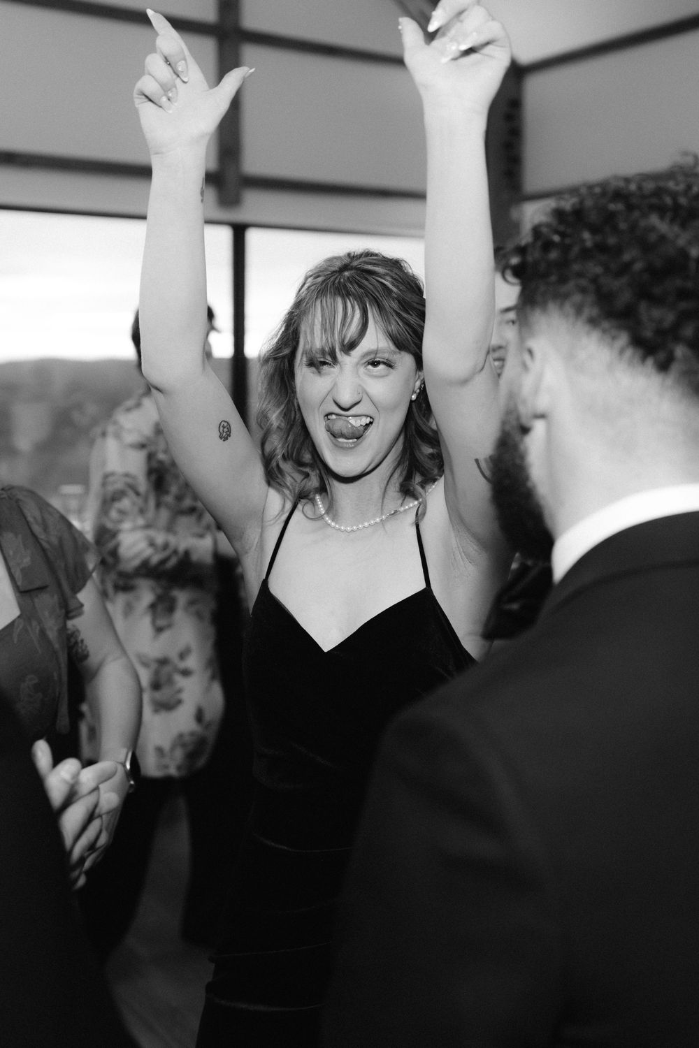Black and white photo of people dancing with raised arms at a celebration or party event.